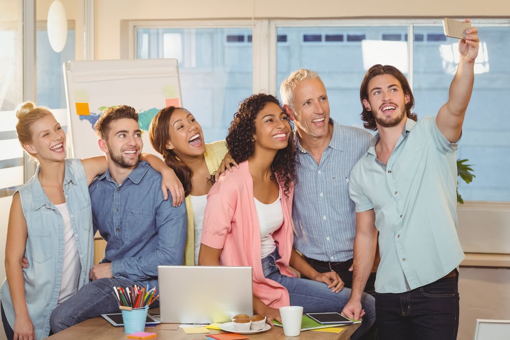 Businessman taking selfie of colleagues in meeting room at creative office